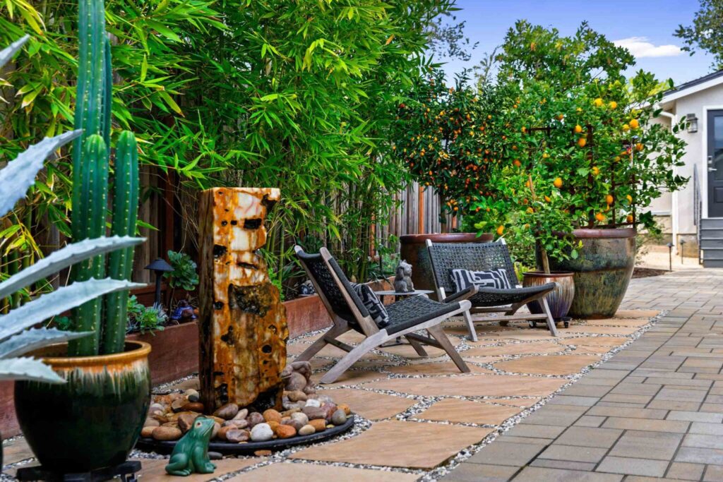 Backyard with mature bamboo and citrus trees, rustic seating area on gravel and paver pathway